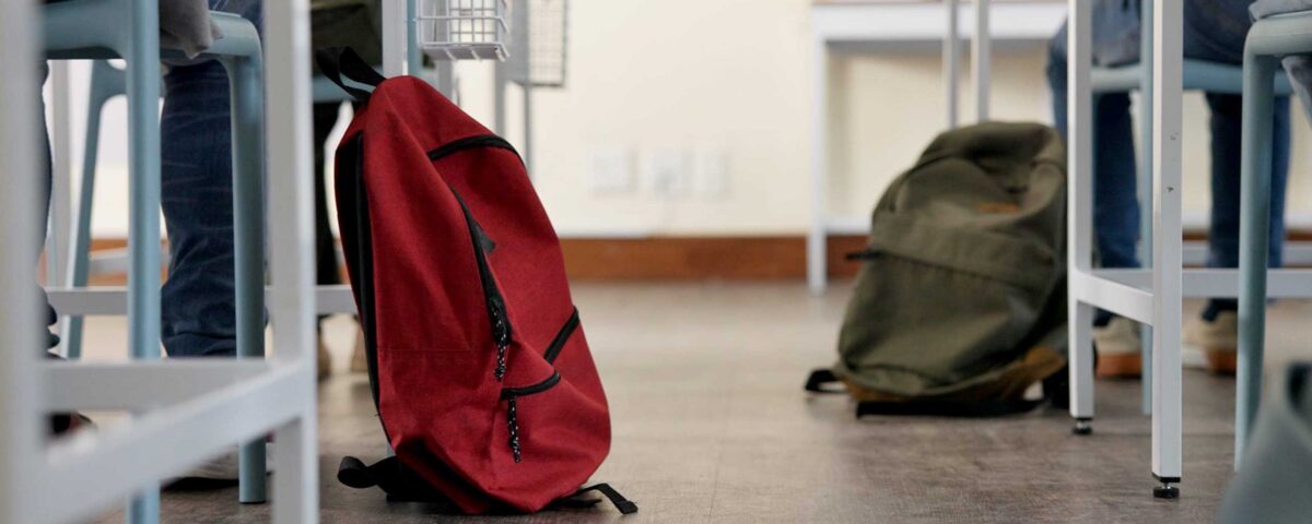 Classroom, backpack and education in school, students and low angle of learning of kids in academy. Desk, legs and children with scholarship, studying and writing of practice exam, bag and knowledge