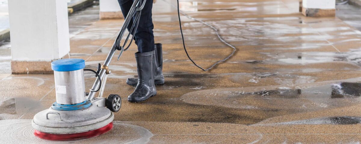 Worker cleaning sand wash exterior walkway using polishing machine and chemical or acid
