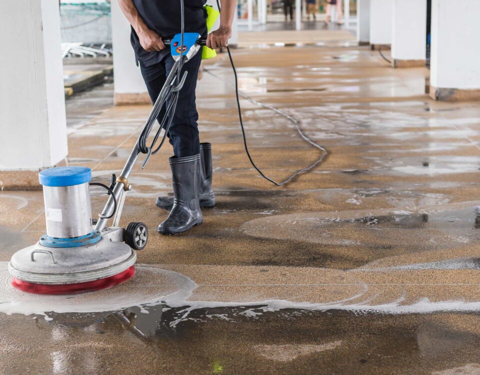 Worker cleaning sand wash exterior walkway using polishing machine and chemical or acid