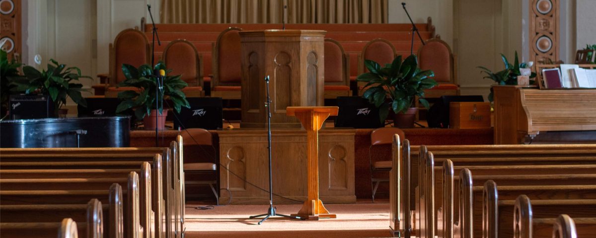 medium wide shot of an empty church sanctuary with afternoon sunlight pouring in creating shadows down the aisle to the front of the church