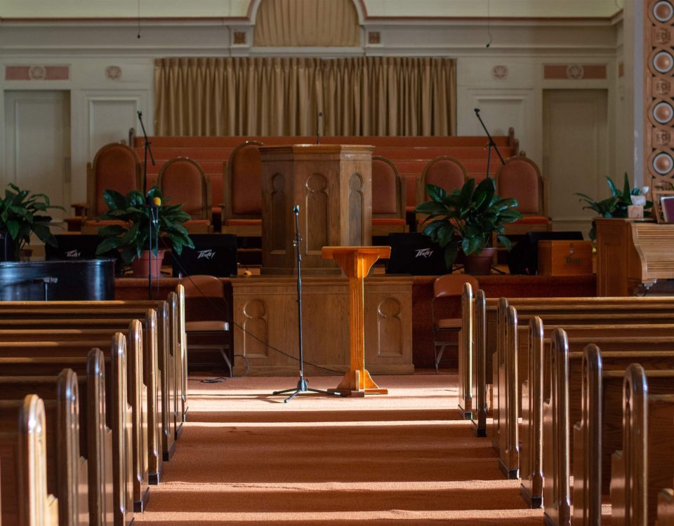 medium wide shot of an empty church sanctuary with afternoon sunlight pouring in creating shadows down the aisle to the front of the church