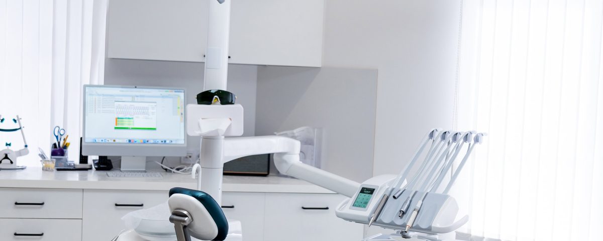 Modern empty dental treatment room with professional medical chair. Interior of a bright clean dental office featuring ergonomic chair, medical equipment, and white cabinet furniture.