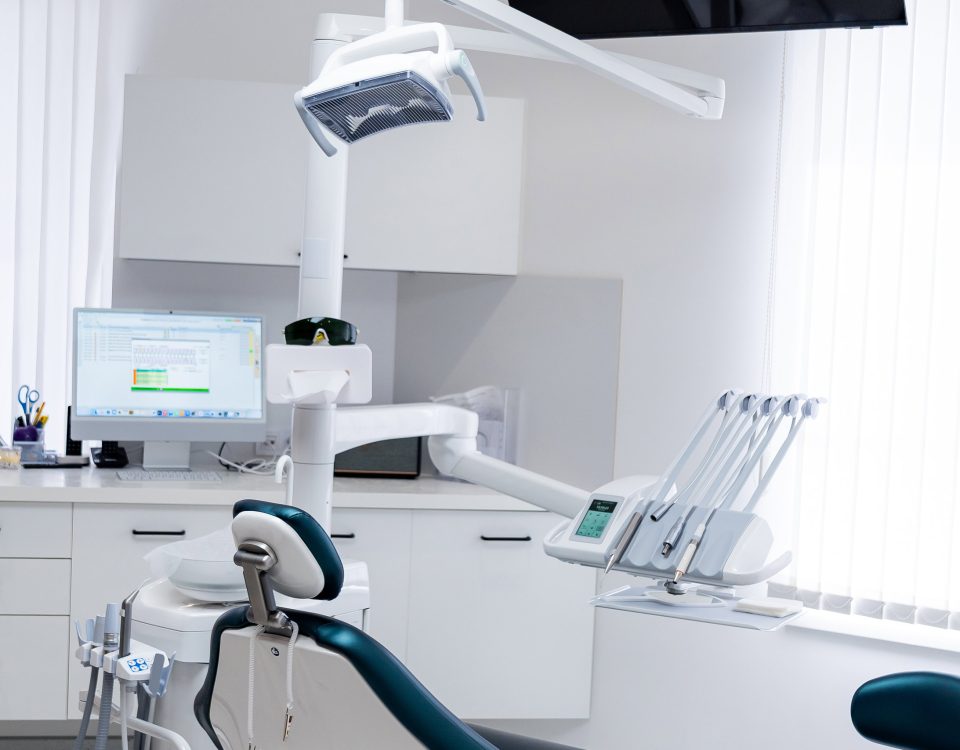 Modern empty dental treatment room with professional medical chair. Interior of a bright clean dental office featuring ergonomic chair, medical equipment, and white cabinet furniture.